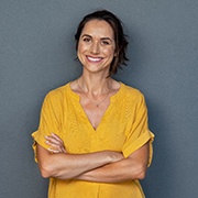 A woman wearing a yellow blouse stands with her arms crossed while smiling and appreciating her new dental implants in Buckhead