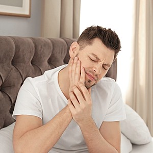 Man in white shirt with oral pain sitting in bed