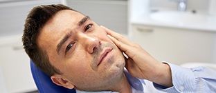 Man in dental chair holding jaw