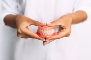 Person in white shirt holding dentures with both hands