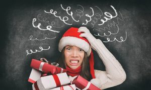 Woman in white sweater and Santa hat holding presents and clenching her teeth